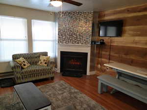 Living room with a fireplace, wood-type flooring, ceiling fan, a baseboard radiator, and wooden walls