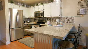 Kitchen featuring white cabinets, kitchen peninsula, appliances with stainless steel finishes, and tasteful backsplash