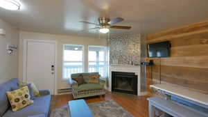 Living room with ceiling fan, wood walls, a textured ceiling, a baseboard heating unit, and hardwood / wood-style floors