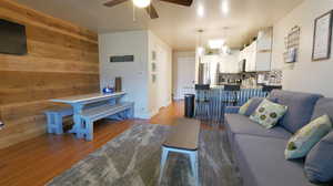 Living room with wooden walls, ceiling fan with notable chandelier, and light wood-type flooring