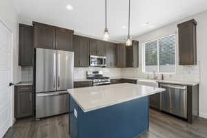Kitchen featuring appliances with stainless steel finishes, decorative backsplash, decorative light fixtures, dark wood-style floors, and dark brown cabinetry