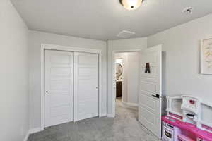 Bedroom with light carpet, a closet, and a textured ceiling