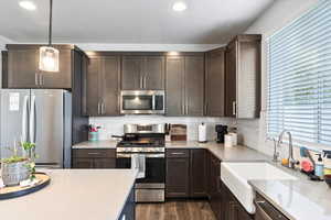 Kitchen featuring dark brown cabinetry, pendant lighting, dark wood-type flooring, appliances with stainless steel finishes, and decorative backsplash