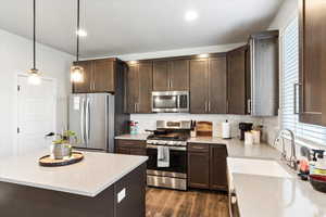 Kitchen featuring hanging light fixtures, sink, backsplash, dark wood-type flooring, and stainless steel appliances