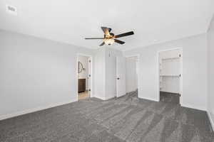 Unfurnished bedroom featuring dark carpet, a walk in closet, ceiling fan, and ensuite bathroom