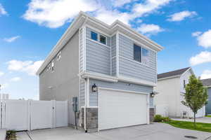View of home's exterior featuring an attached garage, a gate, driveway, and stone siding