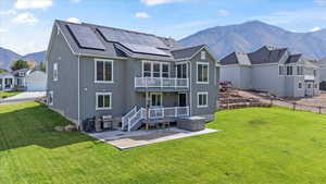 Back of property with a mountain view, a patio area, a yard, a balcony, and solar panels