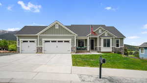 Craftsman-style house featuring stone siding, a garage, a front lawn, driveway, and board and batten siding