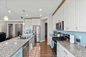 Kitchen with appliances with stainless steel finishes, sink, decorative light fixtures, white cabinets, and dark wood-type flooring