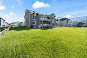 Rear view of house with a lawn, solar panels, and a deck with mountain view