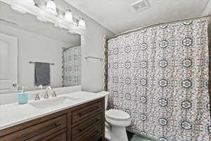 Bathroom with a shower with shower curtain, a textured ceiling, vanity, and toilet