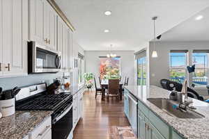 Kitchen with dark wood-type flooring, appliances with stainless steel finishes, white cabinetry, and pendant lighting