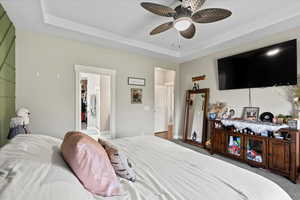 Carpeted bedroom featuring ceiling fan and a raised ceiling