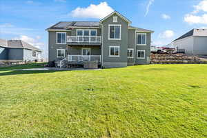 Rear view of house featuring a balcony, solar panels, a wooden deck, a lawn, and cooling unit