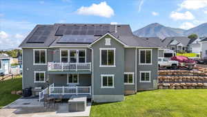 Back of property featuring a patio, a yard, a balcony, solar panels, and a mountain view