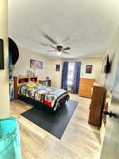 Bedroom with light hardwood / wood-style flooring, ceiling fan, and a textured ceiling