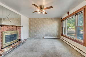 Unfurnished living room featuring a brick fireplace, ceiling fan, baseboard heating, and carpet floors