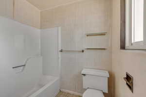 Bathroom with bathtub / shower combination, tile walls, tile patterned flooring, and toilet