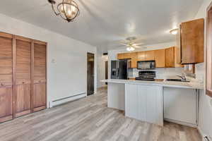 Kitchen featuring sink, hanging light fixtures, baseboard heating, kitchen peninsula, and black appliances