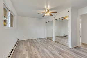 Unfurnished bedroom with ceiling fan, light hardwood / wood-style floors, two closets, and a baseboard radiator