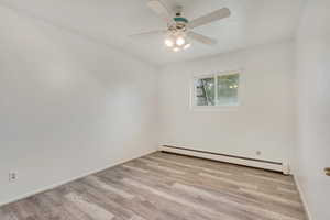 Unfurnished room featuring ceiling fan, light hardwood / wood-style flooring, and a baseboard heating unit