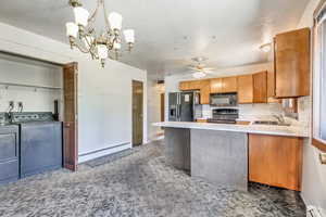 Kitchen with a baseboard heating unit, washer and dryer, sink, ceiling fan with notable chandelier, and appliances with stainless steel finishes