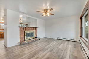 Unfurnished living room with a fireplace, light hardwood / wood-style floors, baseboard heating, and ceiling fan