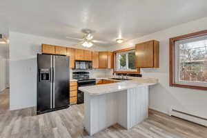 Kitchen featuring black appliances, light hardwood / wood-style flooring, ceiling fan, baseboard heating, and kitchen peninsula