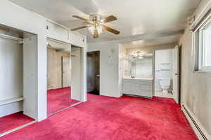 Unfurnished bedroom with carpet flooring, ceiling fan, a baseboard heating unit, and ensuite bathroom