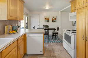 Kitchen with light brown cabinetry, backsplash, white appliances, and kitchen peninsula