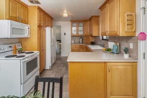 Kitchen featuring tasteful backsplash, kitchen peninsula, sink, white appliances, and a textured ceiling