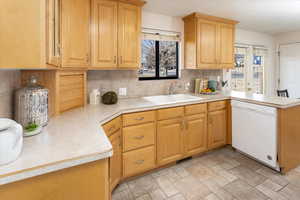 Kitchen featuring kitchen peninsula, white dishwasher, backsplash, and sink