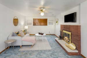 Living room featuring ceiling fan, a fireplace, and carpet flooring