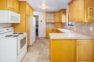 Kitchen with backsplash, white appliances, sink, and kitchen peninsula