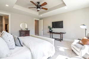 Bedroom featuring a raised ceiling, ceiling fan, and light colored carpet