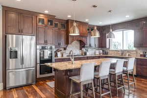 Kitchen with light stone counters, appliances with stainless steel finishes, dark hardwood / wood-style floors, and a kitchen island