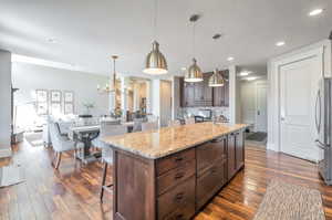 Kitchen featuring a textured ceiling, dark wood-type flooring, a breakfast bar area, a center island with sink, and decorative light fixtures