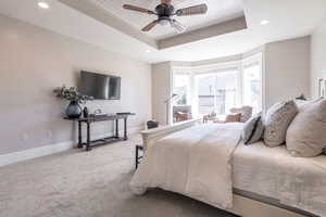 Bedroom with ceiling fan, a tray ceiling, and carpet