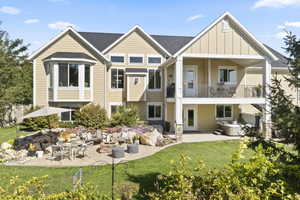 Back of house featuring a lawn, a balcony, a hot tub, and a patio area