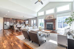 Living room with ceiling fan with notable chandelier, high vaulted ceiling, dark hardwood  floors, and plenty of natural light