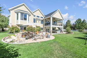 Rear view of property with a balcony, ceiling fan, a patio area, and a lawn