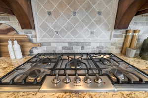 Room details with light stone countertops, backsplash, and stainless steel gas cooktop