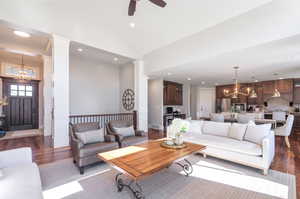 Living room featuring ornate columns, ceiling fan with notable chandelier, dark wood flooring, and high vaulted ceiling