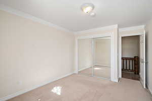 Unfurnished bedroom featuring light carpet, a textured ceiling, a closet, and crown molding