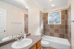 Full bathroom with ornamental molding, vanity, tiled shower / bath combo, and toilet