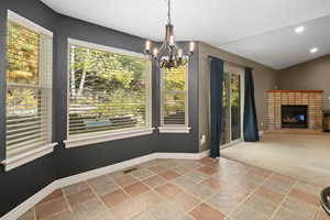 Unfurnished dining area with a brick fireplace, a chandelier, carpet, and a wealth of natural light