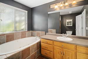 Bathroom with a relaxing tiled tub, vanity, tile patterned flooring, and toilet