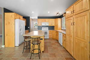 Kitchen featuring light brown cabinets, sink, white appliances, a center island, and a kitchen bar