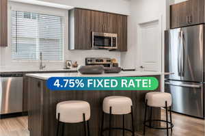 Kitchen with appliances with stainless steel finishes, dark brown cabinets, a breakfast bar area, and light hardwood / wood-style flooring