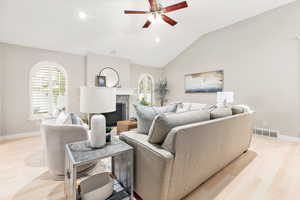 Living room featuring a fireplace, light hardwood / wood-style floors, vaulted ceiling, and ceiling fan